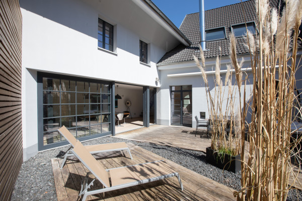Sonnenliegen auf der Terrasse mit Schilfbepflanzung und Blick zur großen Schiebetür des Essbereichs