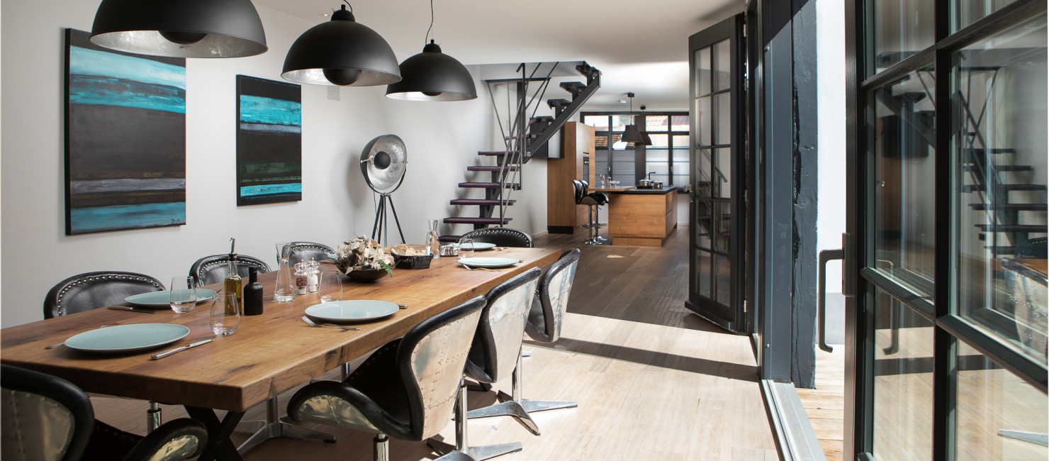 Moderner Esstisch mit STühlen und dunklen Hängelampen mit Blick richtung Küche und offener Treppe