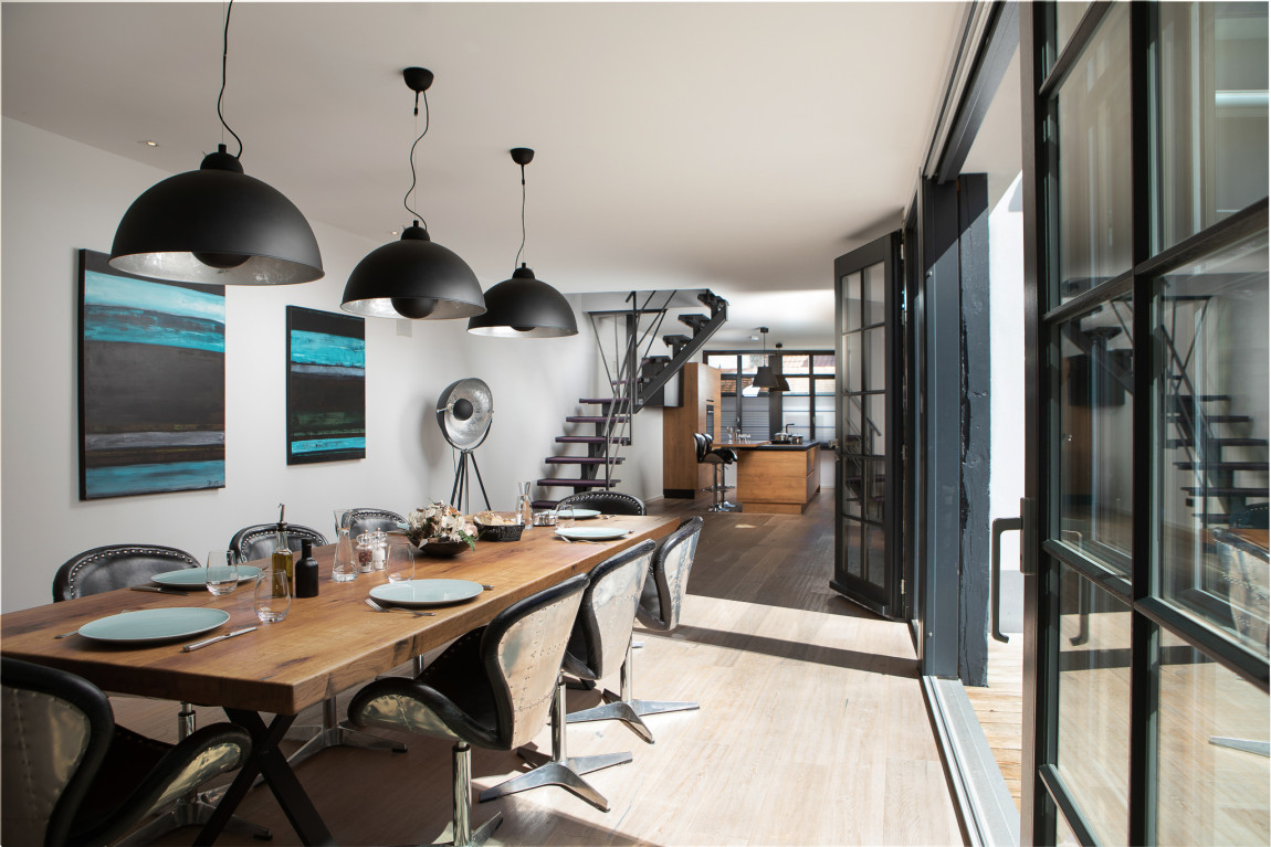Großer Esstisch aus Holz mit modernen Stühlen mit Metalllehne, alles in Holz, schwarz und weiß gehalten im Hintergrund Blick zur offenen Küche