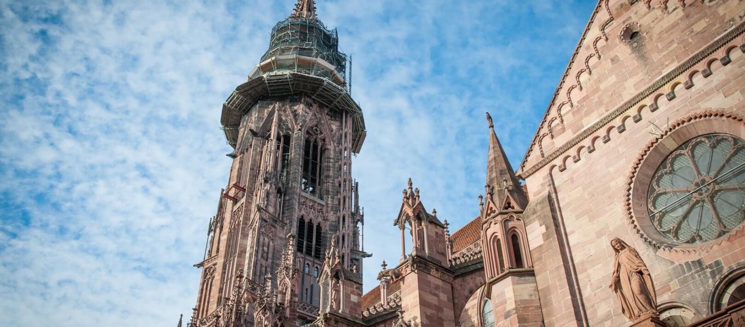 Blick auf die Spitze eines historischen Kirchturms in Freiburg bei blauem Himmel 